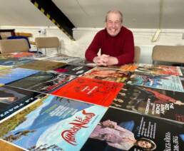 John Acton sitting in front of a number of music albums that he sold on eBay.