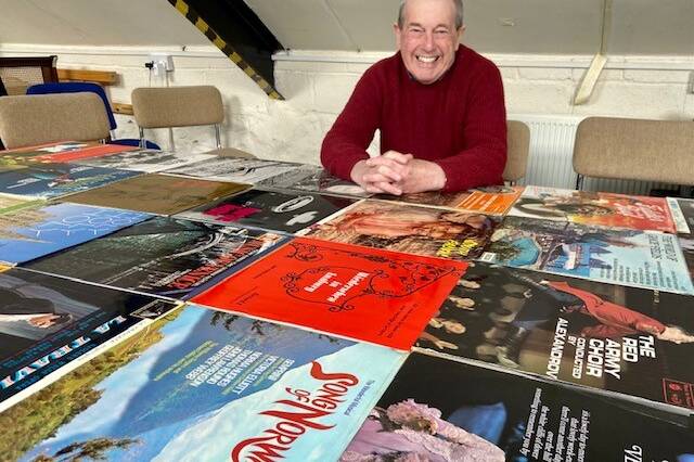 John Acton sitting in front of a number of music albums that he sold on eBay.