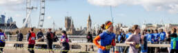 People running across a bridge in London with the London eye and parliment building in the background.