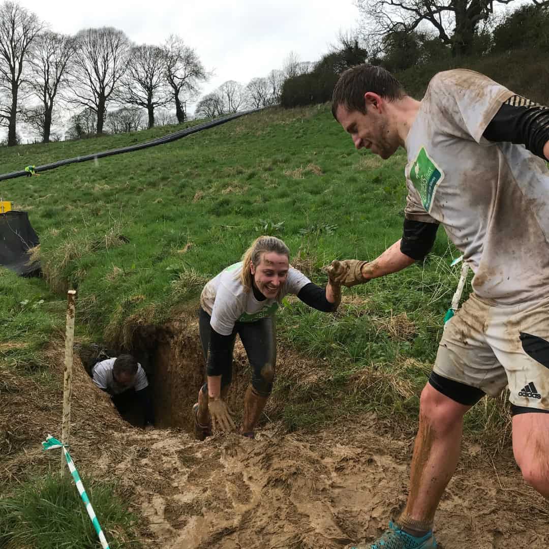 man helping a woman climb out of a muddy tunnel.