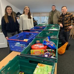 4 volunteers standing next to crates. They are sorting through donated things.